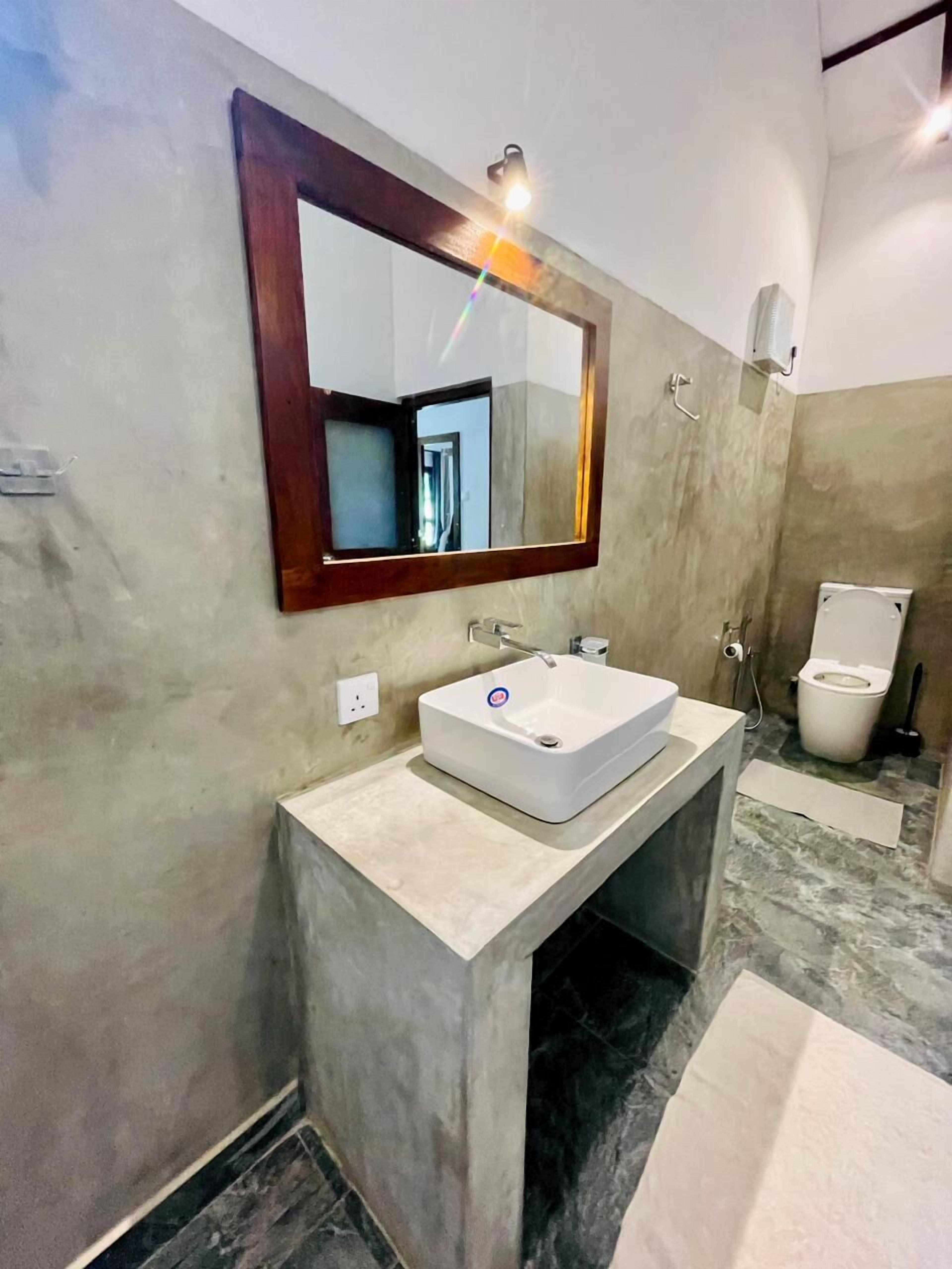 Une salle de bain avec un lavabo rectangulaire, un miroir avec un cadre en bois, des toilettes et un espace douche.