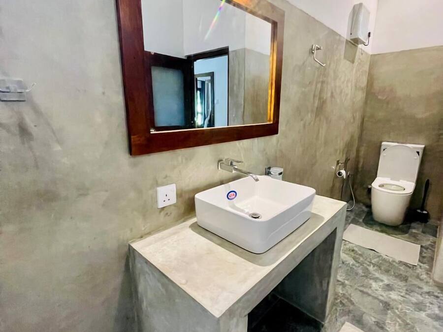 Une salle de bain avec un lavabo rectangulaire, un miroir avec un cadre en bois, des toilettes et un espace douche.