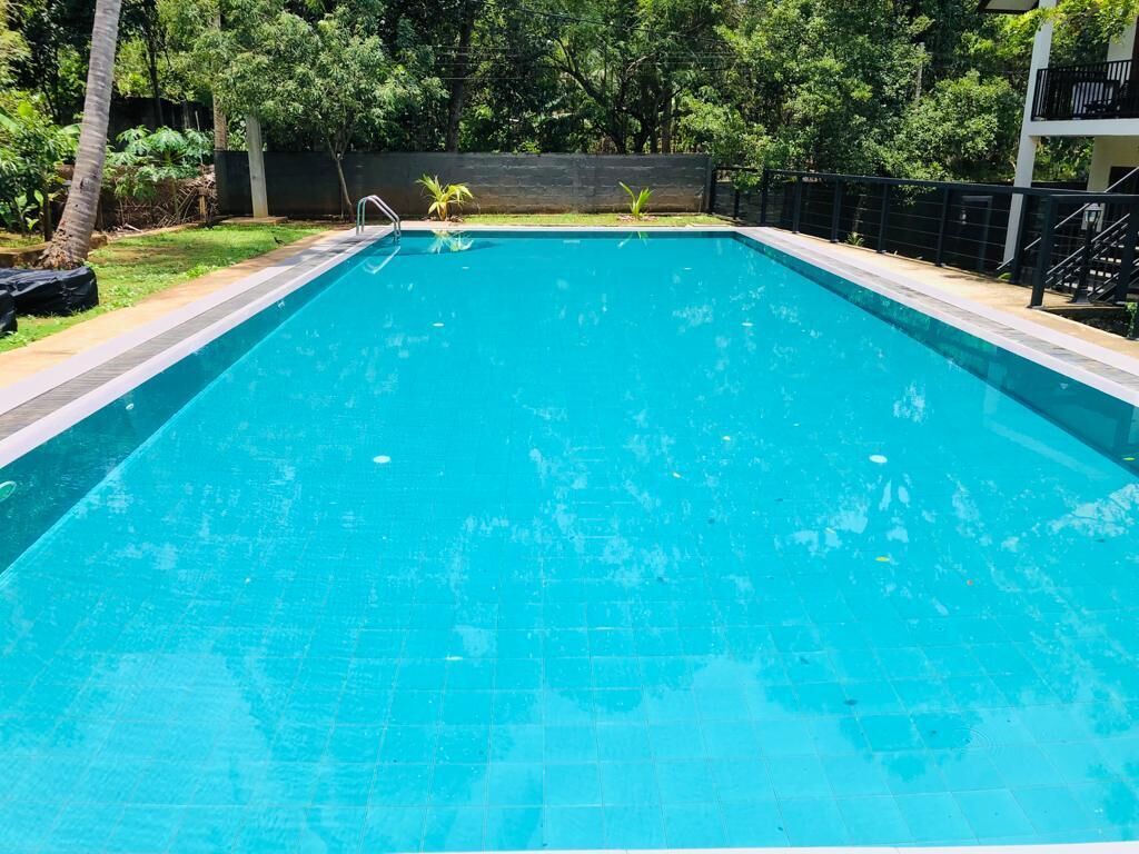 A rectangular swimming pool with a tiled edge, surrounded by a low wall and a metal railing.