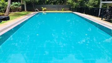 A rectangular swimming pool with a tiled edge, surrounded by a low wall and a metal railing.