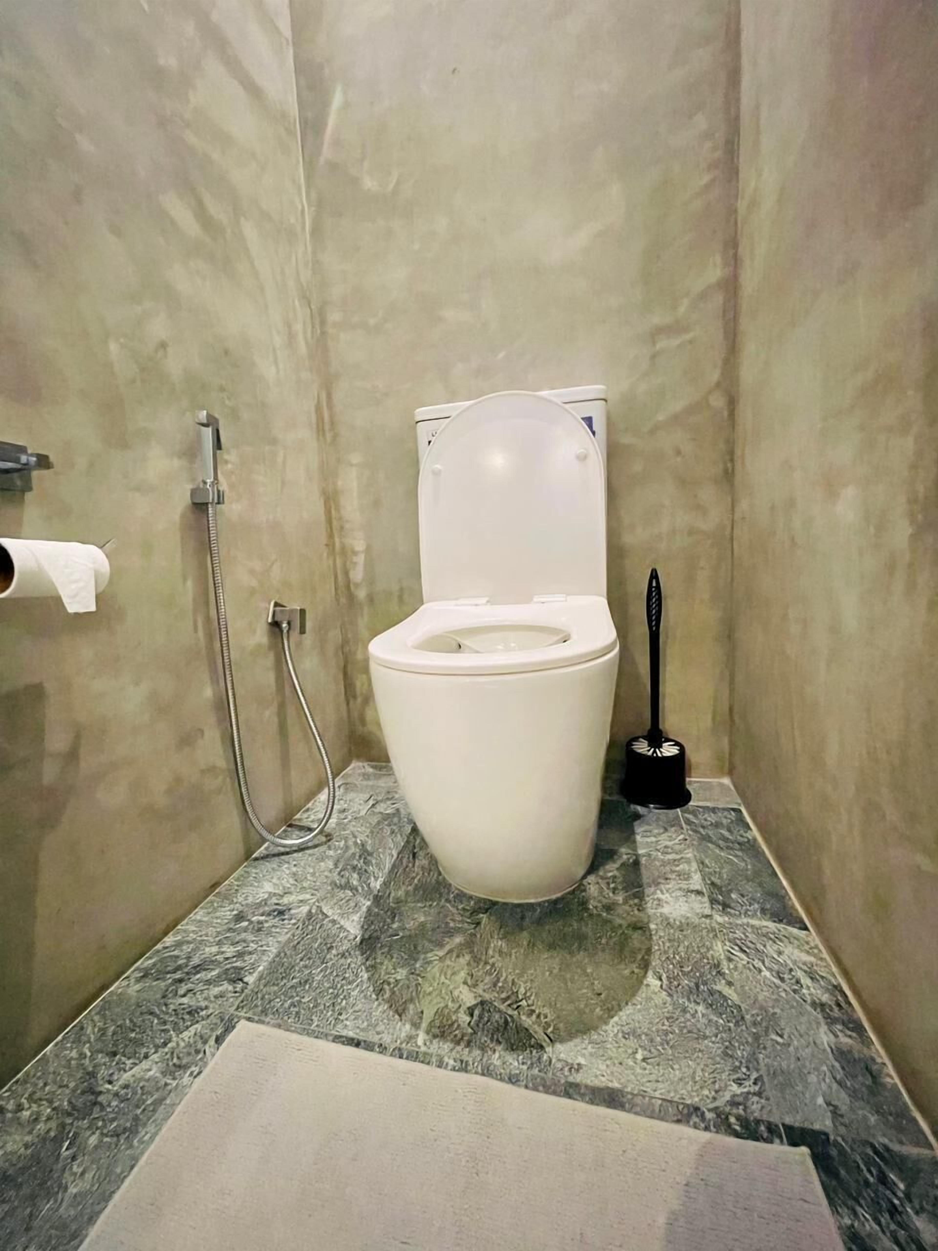 A bathroom with a toilet, a handheld showerhead, and a toilet brush.