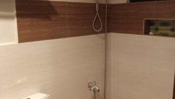 A small bathroom with a shower, toilet, and a wooden shelf above the toilet.