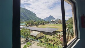 A view from a window overlooking a campus with buildings, a sports field, and mountains. - Amos Pili Tree Inn powered by Cocotel (El Nido)