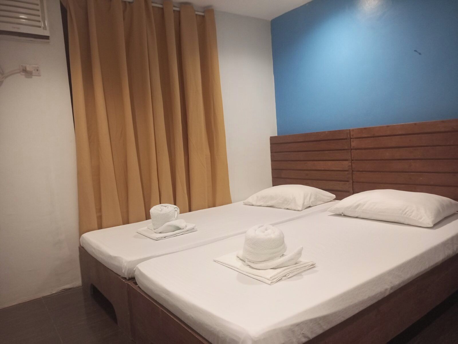 Un lit double avec du linge de lit et des serviettes blanches, une tête de lit en bois et un mur d’accent bleu.
