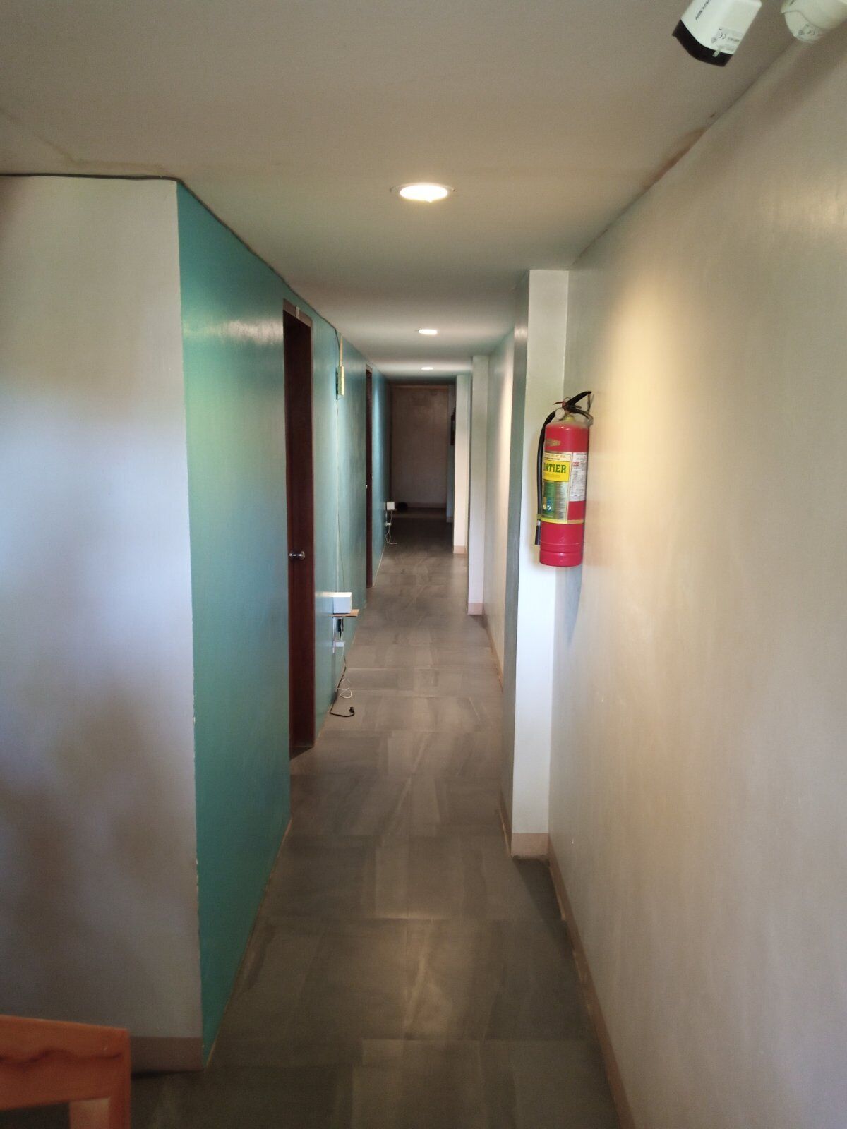 Een gang met turquoise wanden, een aan de muur bevestigd brandblusser en een betegelde vloer.