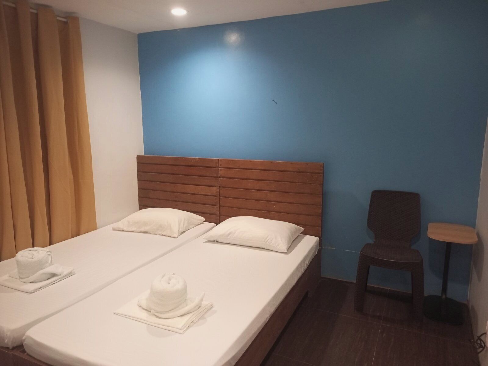 A hotel room with a double bed, two pillows, a wooden headboard, a small round table, and a chair.
