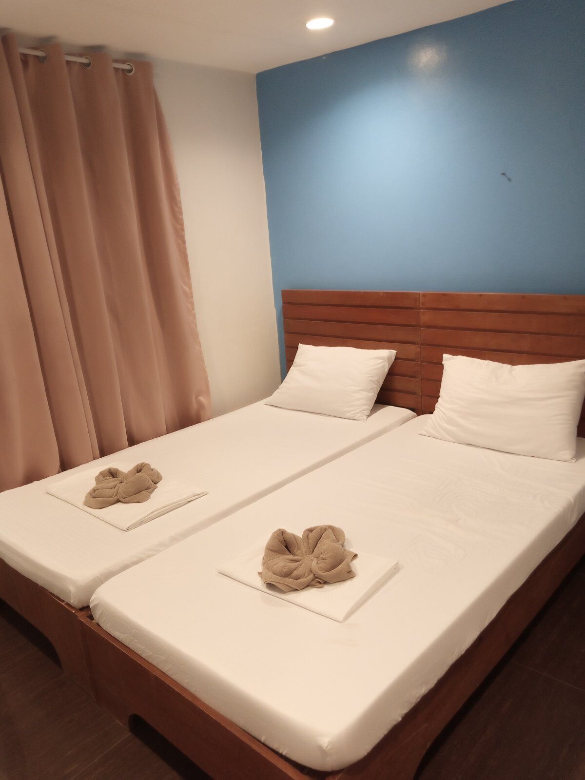 A double bed with two pillows, a wooden headboard, and a beige blanket folded on the bed.