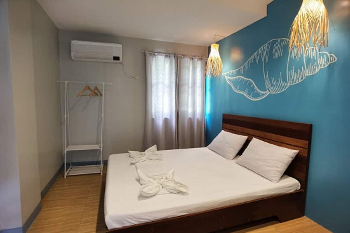 A neatly made bed with white linens and towels, a wooden headboard, and a wall-mounted air conditioner.