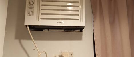 A white Carrier air conditioner mounted on a wall with a power cord plugged into a wall socket.