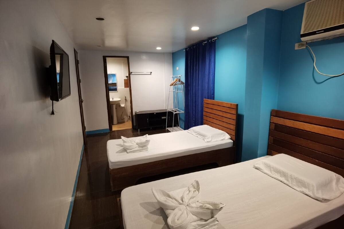 A hotel room with two beds, a TV, a wardrobe, and an air conditioning unit.