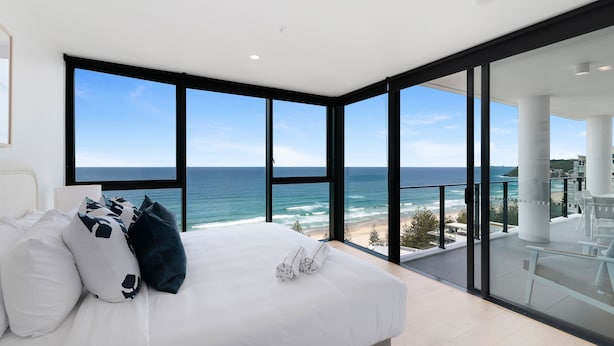 A bedroom with a large bed, white bedding, and a view of the ocean through floor-to-ceiling windows. - Sandbar Burleigh (Burleigh Heads)