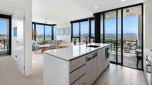 A modern kitchen with a large island, a dining area with a round table, and a balcony with a city view. - Sandbar Burleigh (Burleigh Heads)