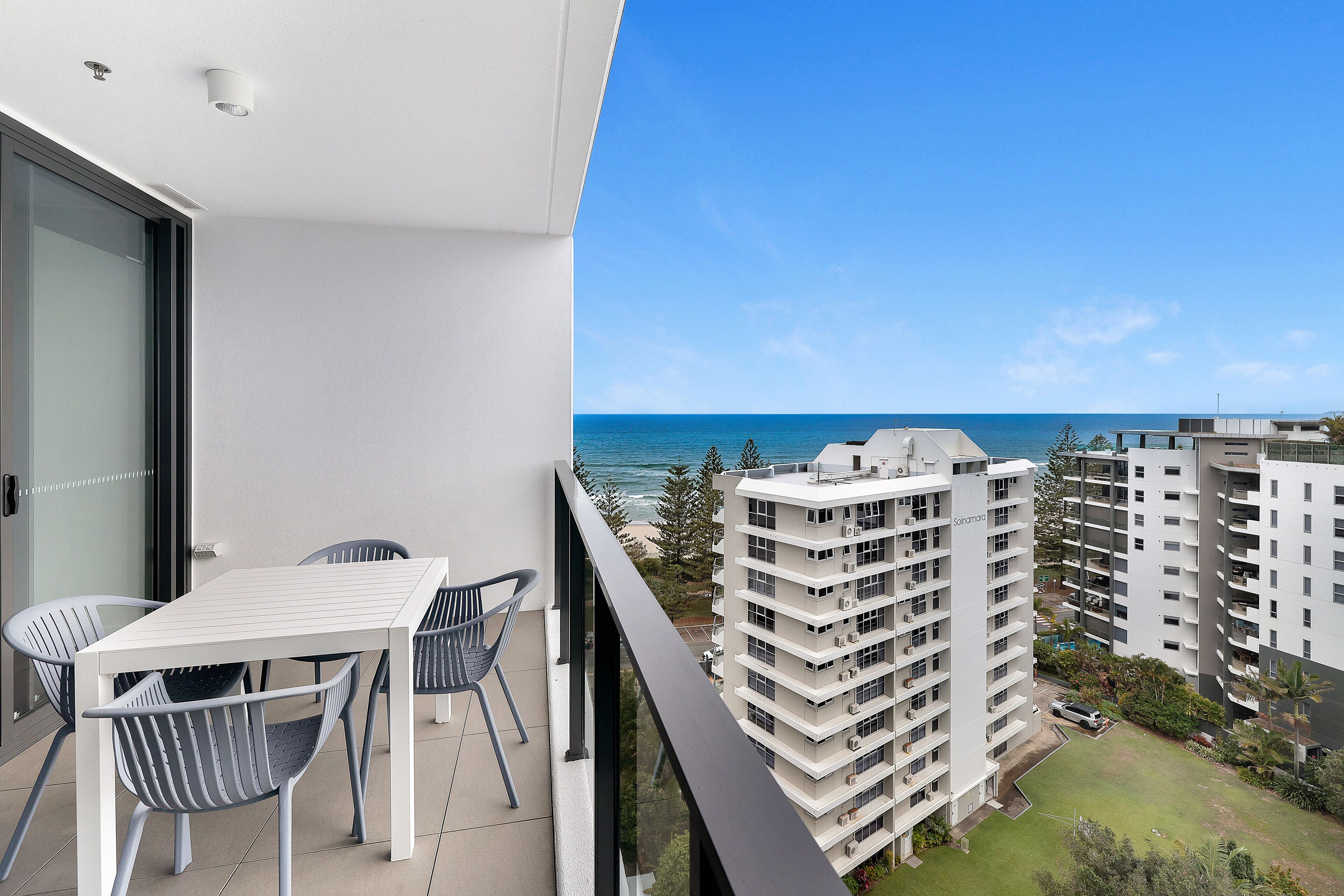 A balcony with a table and chairs, overlooking a beach and high-rise buildings.