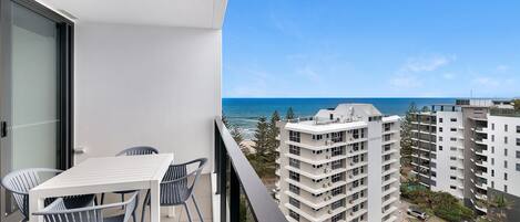 A balcony with a table and chairs, overlooking a beach and high-rise buildings.