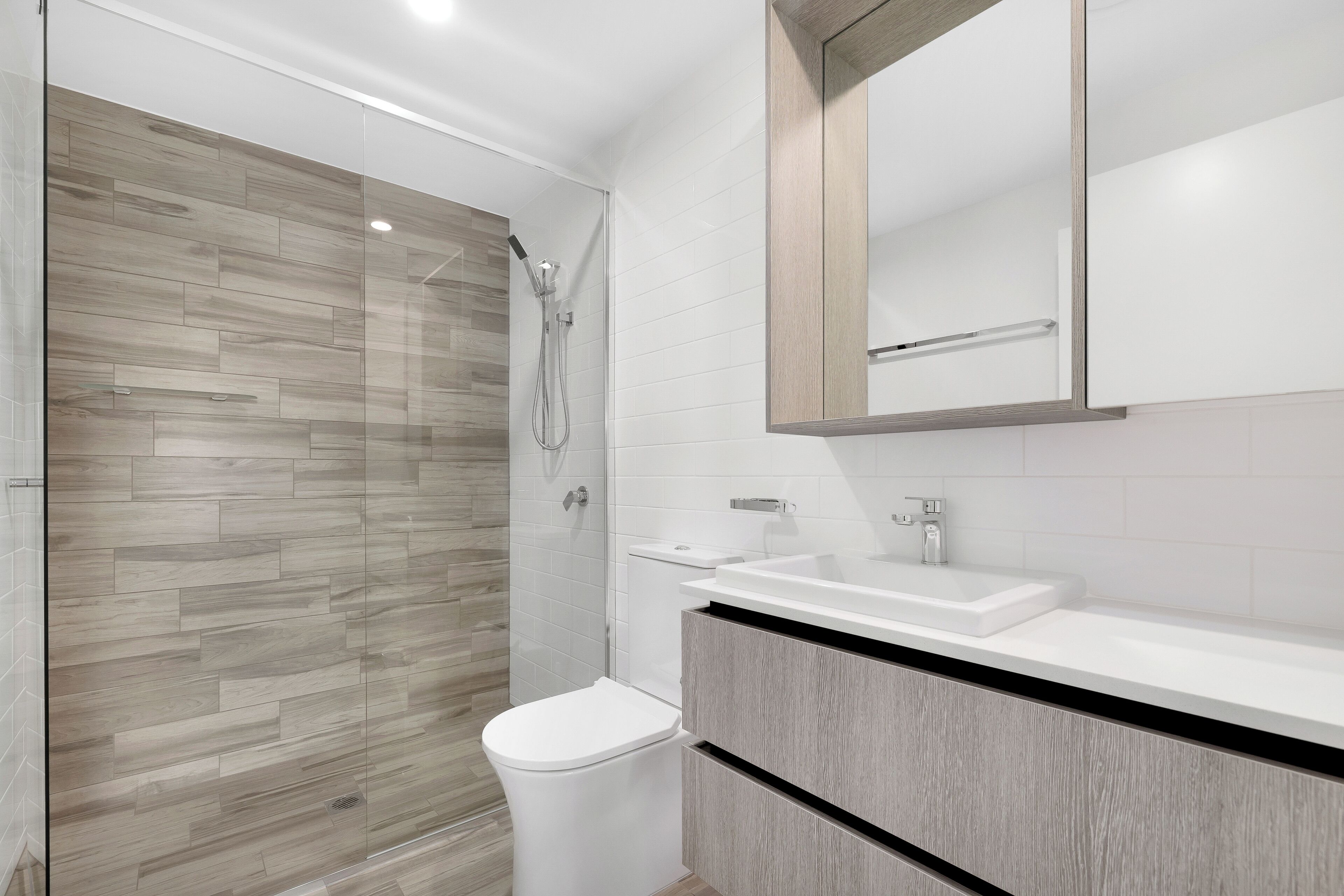 A modern bathroom with a glass shower enclosure, a white toilet, and a vanity with a mirror.