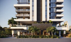 Un hotel moderno con varios balcones, un elemento vertical central y abundante vegetación.