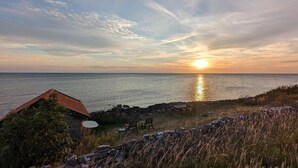 A sunset view over the ocean with a stone wall and a small building with a red roof. - Stunning home in Borgholm with WiFi (Borgholm)
