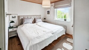 A bedroom with a large bed, a bedside table with a lamp, a window with a view of greenery, and a ceiling fan. - Stunning home in Borgholm with WiFi (Borgholm)