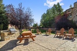 Un patio con tavolo da picnic e poltrone Adirondack, un barbecue in pietra e un muro in pietra.