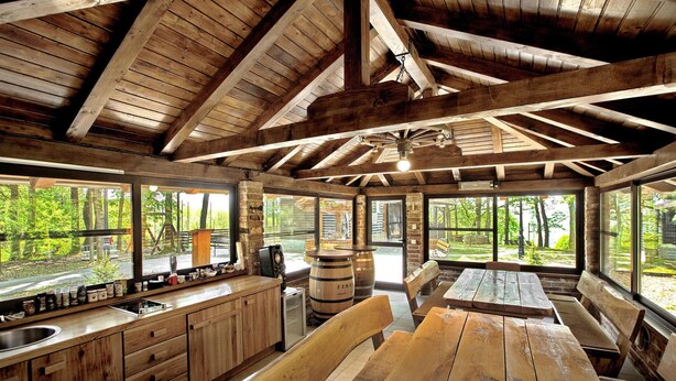 A rustic wooden cabin with a kitchen area, wooden tables and benches, and large windows offering views of a forested area. - Gorgeous home in Gustelnica with sauna (Gustelnica)