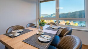 A dining area with a table set for four, large windows with a mountain view, and a modern ceiling light fixture.
