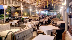An outdoor restaurant with multiple tables and chairs, a thatched roof, and hanging lights. - Honiara Hotel (Honiara)