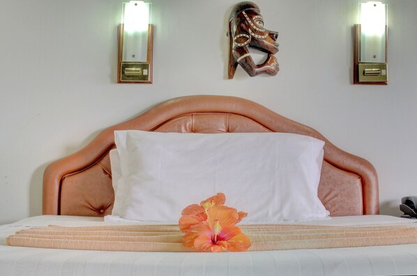 A bed with a headboard, a white pillow, a white bedsheet, and an orange hibiscus flower. - Honiara Hotel (Honiara)