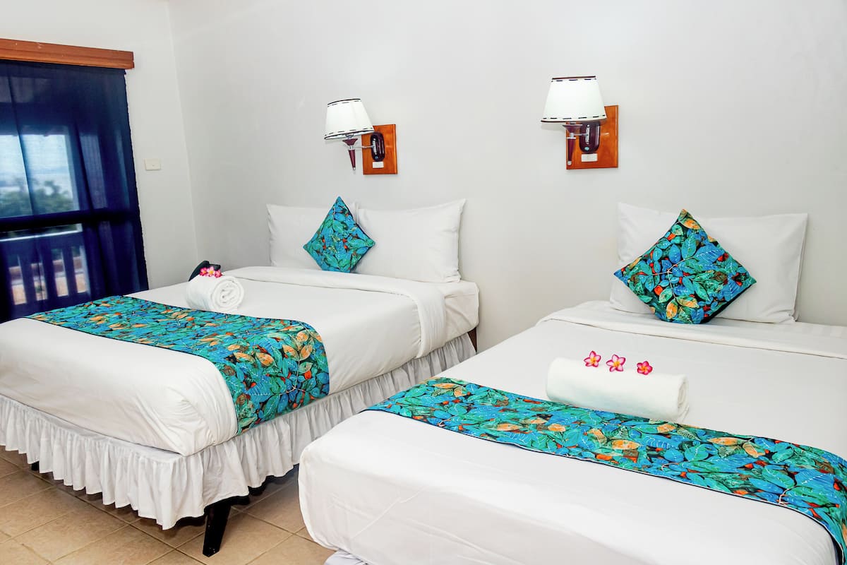 Two beds with white linens, blue floral bedspreads, and decorative pillows.