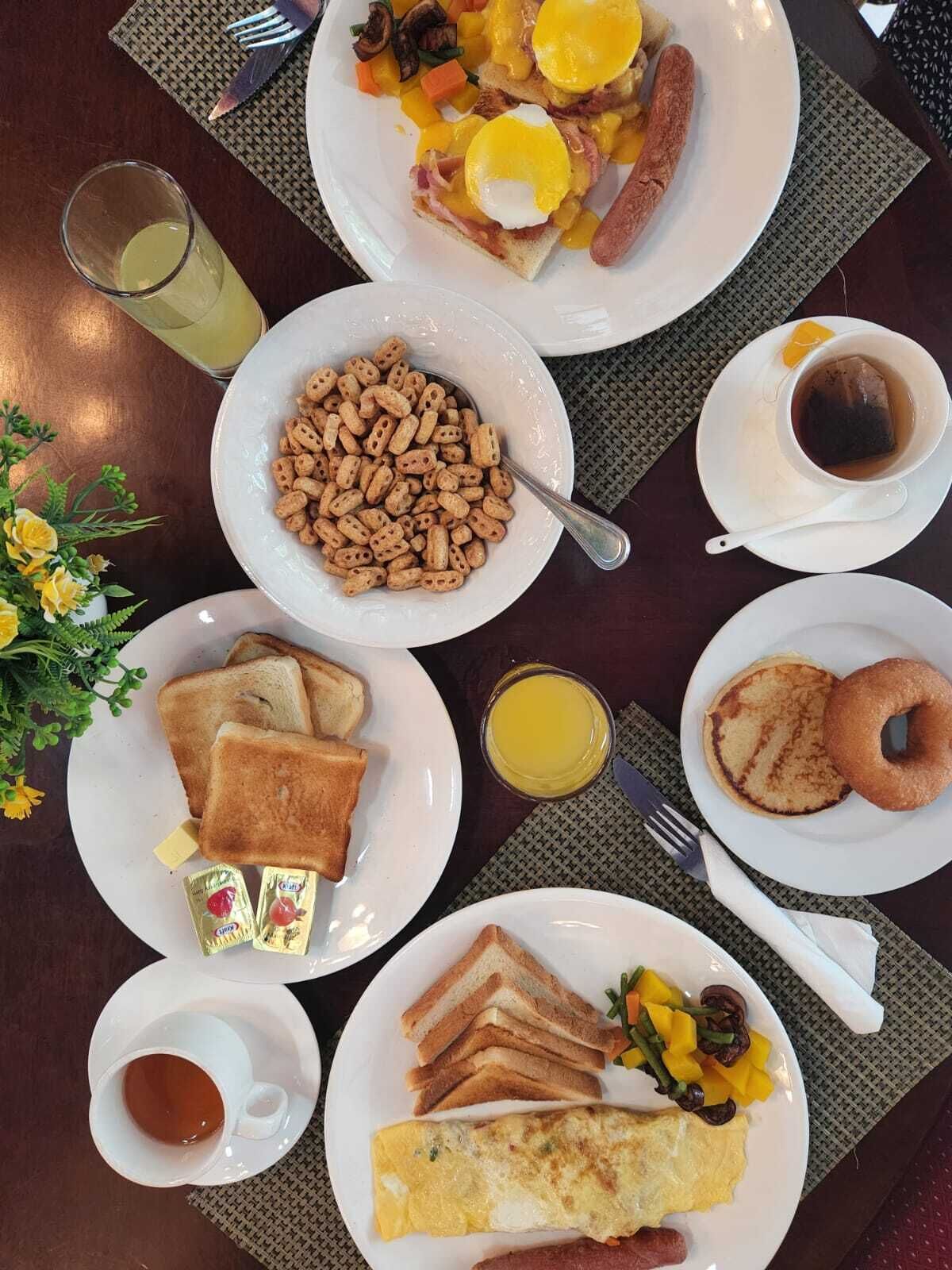 Une table mise pour le petit-déjeuner, avec des assiettes de pain grillé, des œufs, des saucisses et un bol de céréales.