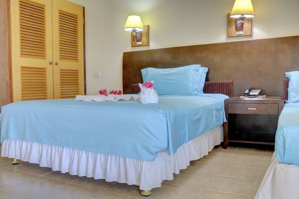 A hotel room with a large bed, a nightstand, a wooden wardrobe, and two wall-mounted lamps.
