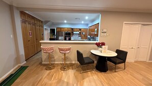 Een moderne keuken met houten kastjes, een centraal eiland en een eethoek met twee roze barstoelen en twee zwarte stoelen.