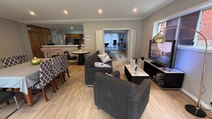 Een moderne woonkamer met een eethoek, een keuken op de achtergrond en een grote televisie aan de rechterkant.
