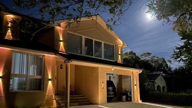 Een woonhuis met twee verdiepingen en een garage, verlicht door buitenverlichting.
