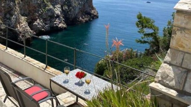 A seaside terrace with a table and chairs, overlooking the sea and a rocky cliff with a tower. - Villa Kolorina (Dubrovnik)