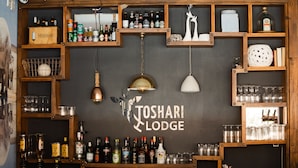 A bar area with shelves of liquor bottles, glasses, and a chalkboard sign reading "JOSHARI LODGE".