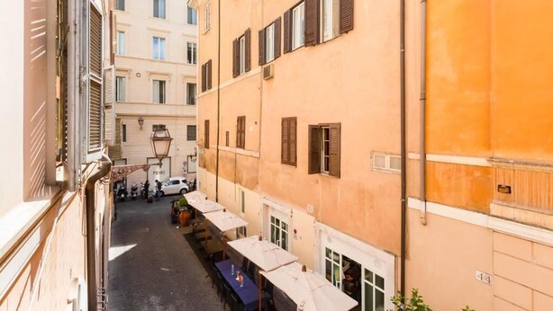 A narrow street with buildings on either side, outdoor seating for a café, and a parked car. - Premium Private Suites (Rome)
