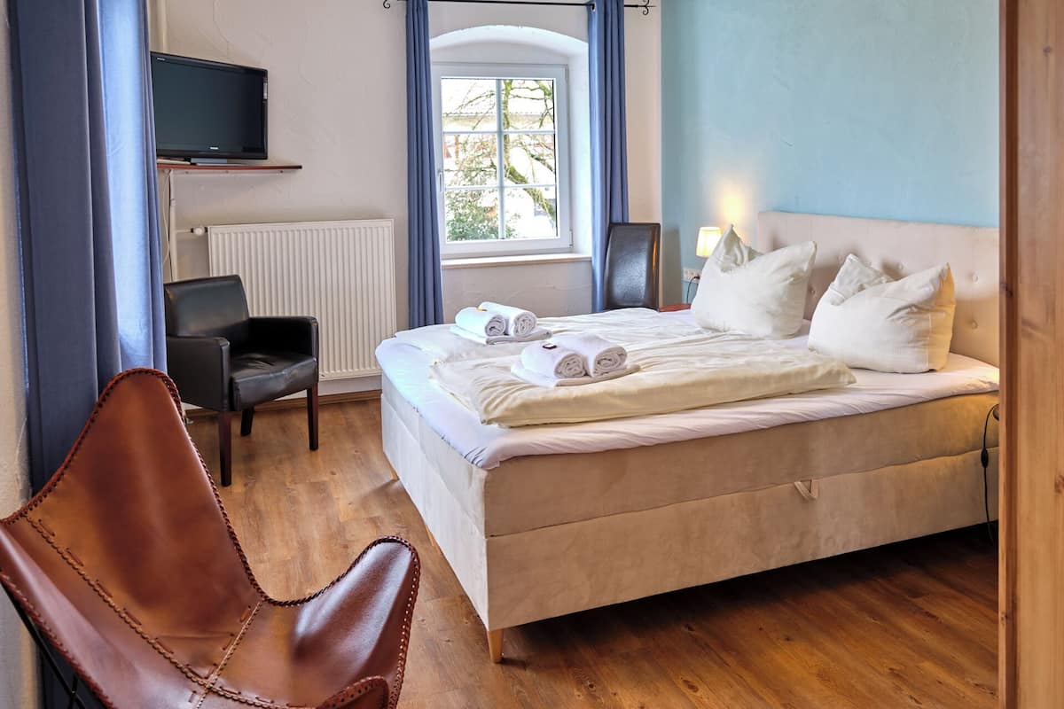 Habitación de hotel con cama, una silla, televisor y ventana con cortinas.