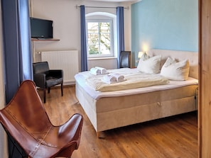 Ein Hotelzimmer mit Bett, Sessel, Fernseher und einem Fenster mit Vorhängen.