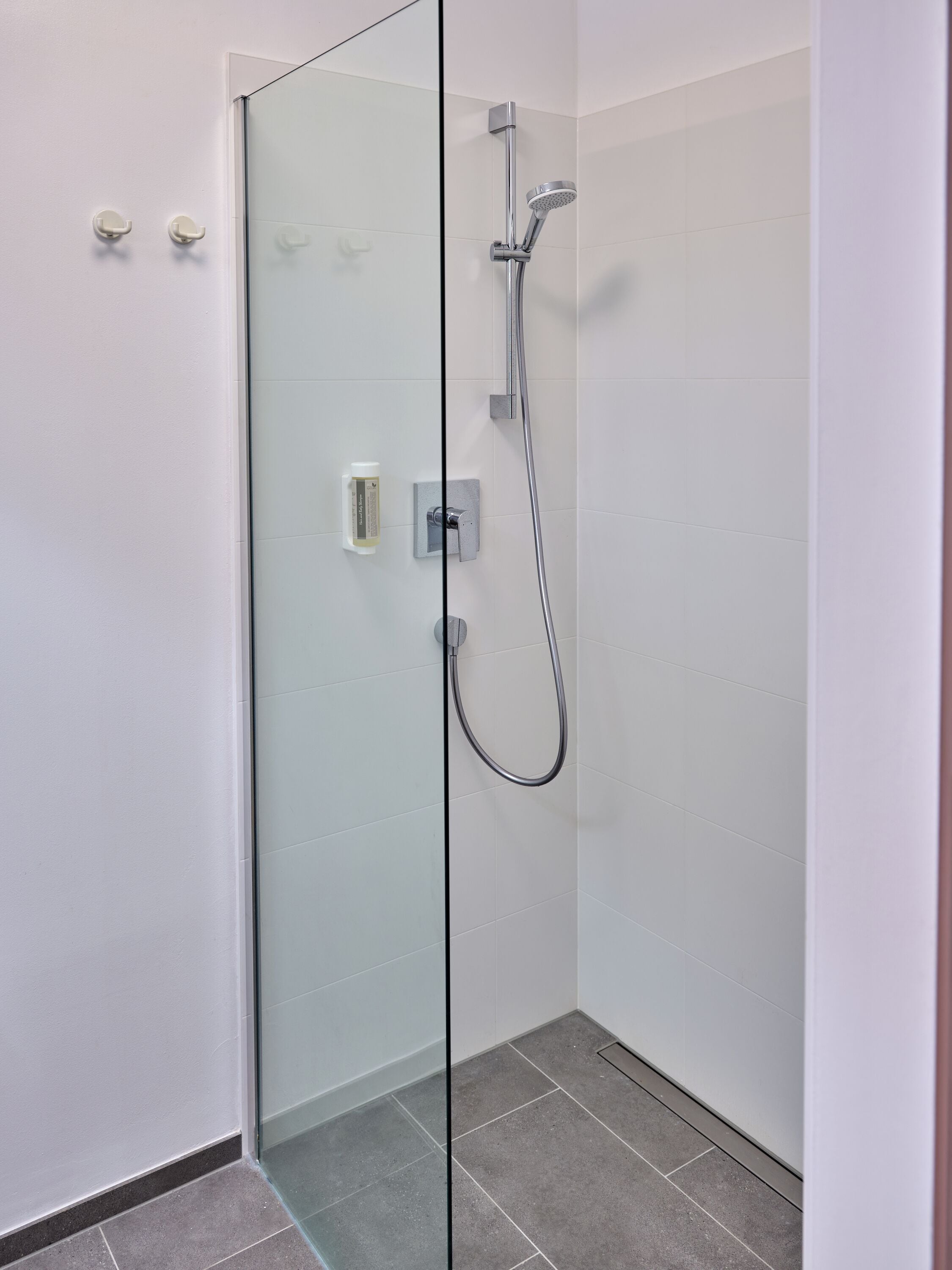 Una ducha moderna con puerta de vidrio, un cabezal de ducha manual y un panel de control en la pared.