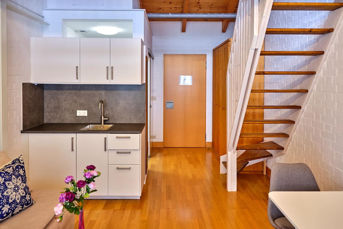 Cocina compacta con armarios blancos, encimera de madera y una escalera de madera.