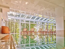 Un amplio espacio interior con techo de vidrio que deja entrar luz natural, y una fila de sillas de madera frente a un piso reflectante.
