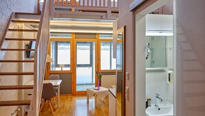 Un interior moderno con una escalera de madera, una pequeña mesa con un florero y un baño con lavamanos y espejo.