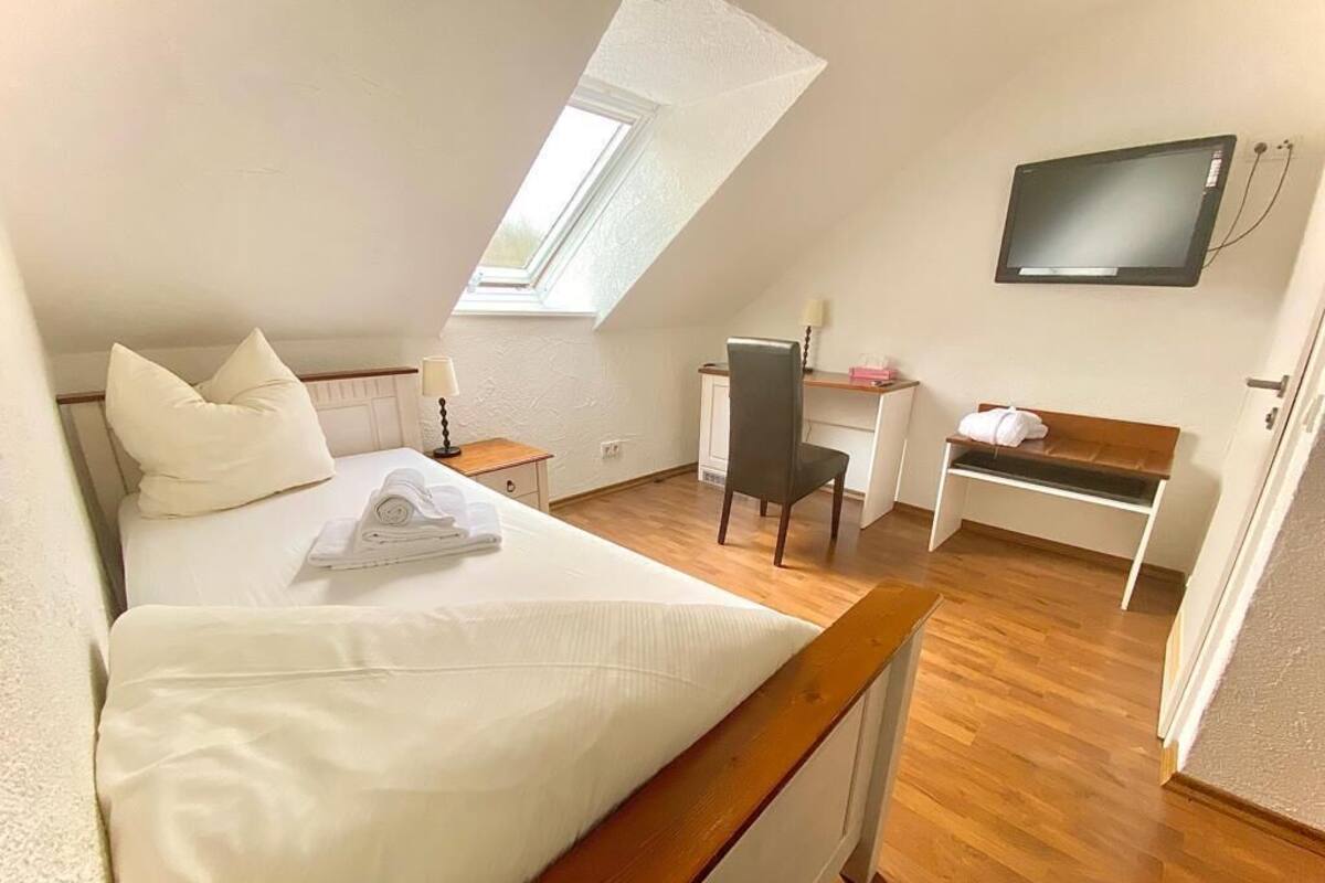Un dormitorio con cama, escritorio, silla, televisor y ventana.