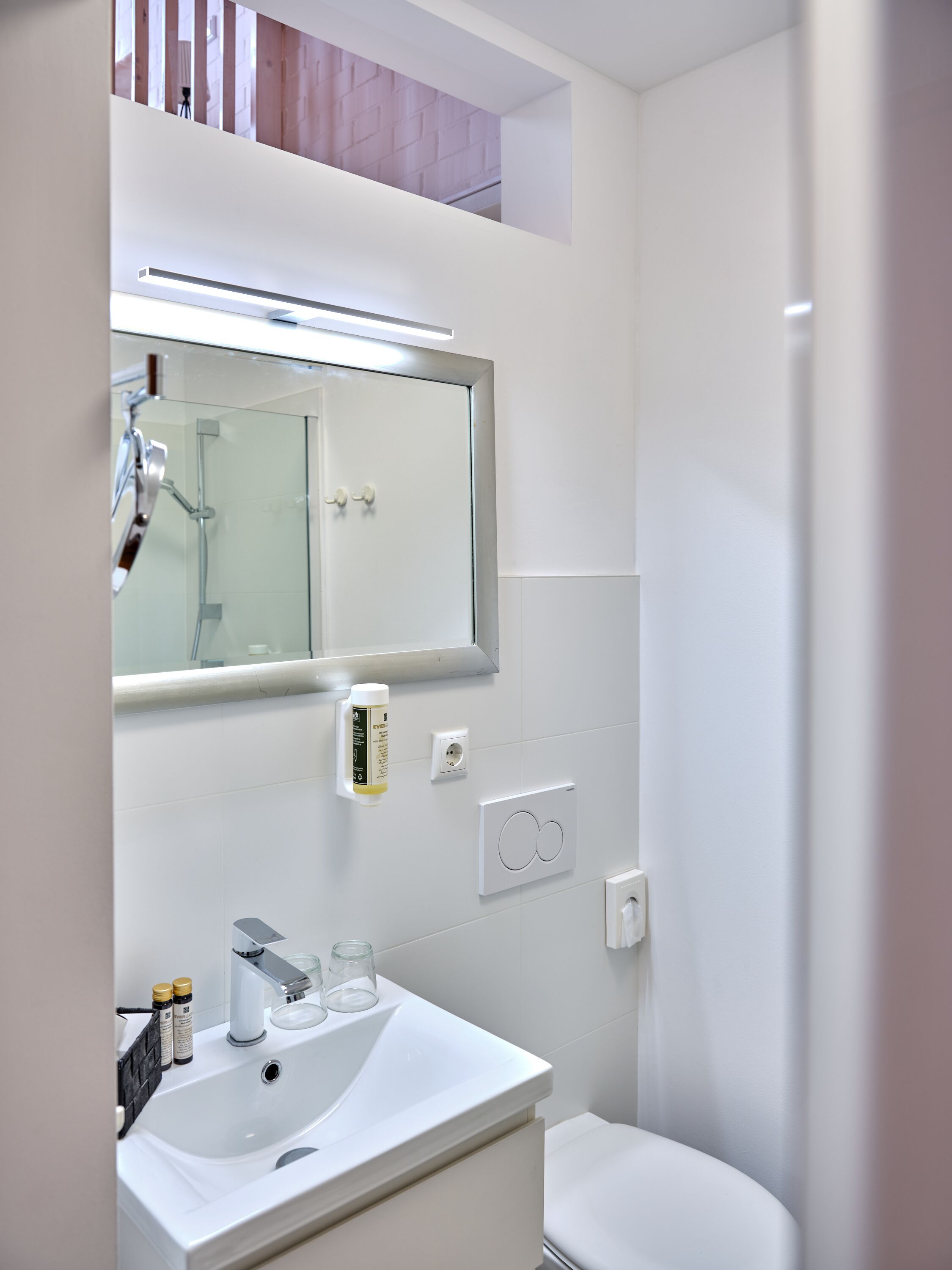Un baño moderno con un lavamanos blanco, un espejo, una ducha y un inodoro.