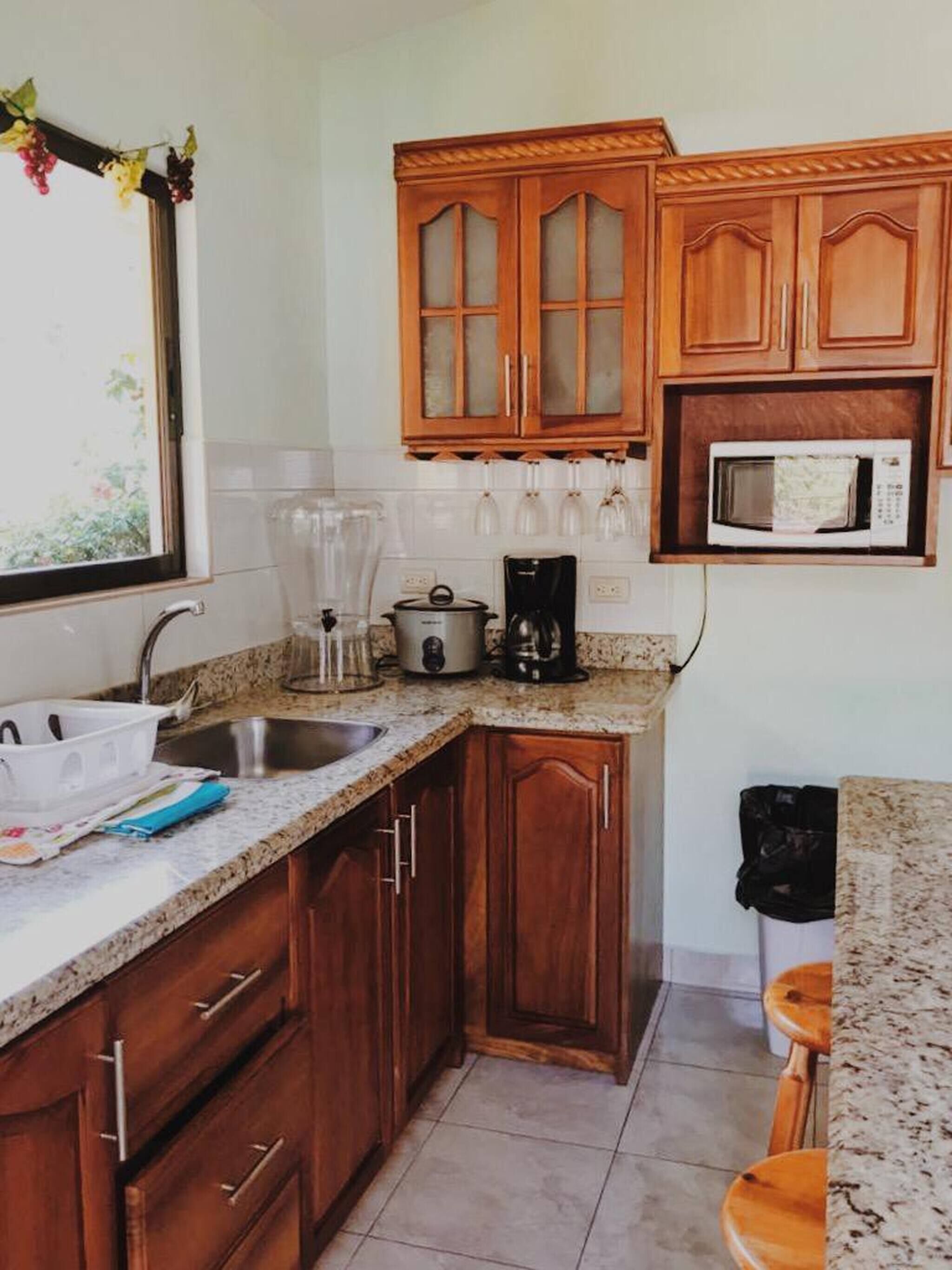 Una cocina con armarios de madera, un lavamanos, una cafetera y un microondas.