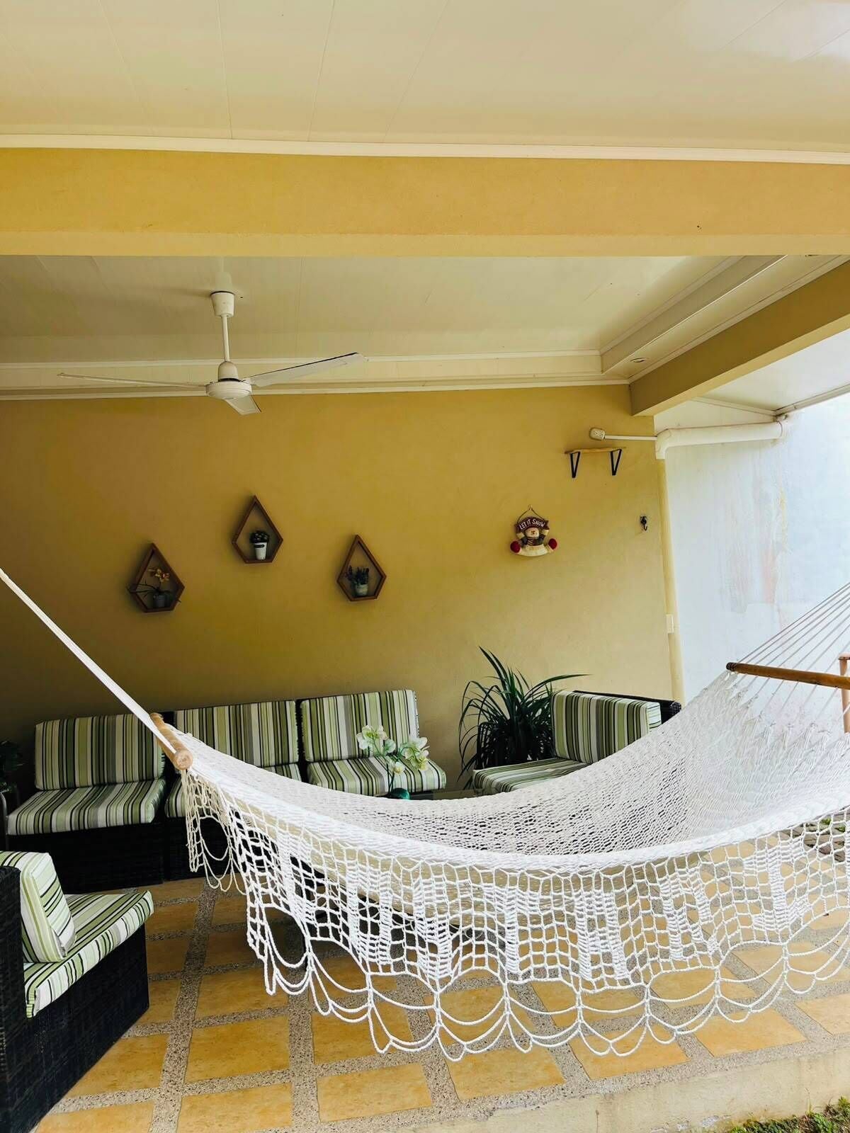 A hammock suspended over a tiled floor, a striped sofa, and a ceiling fan in a room with yellow walls.