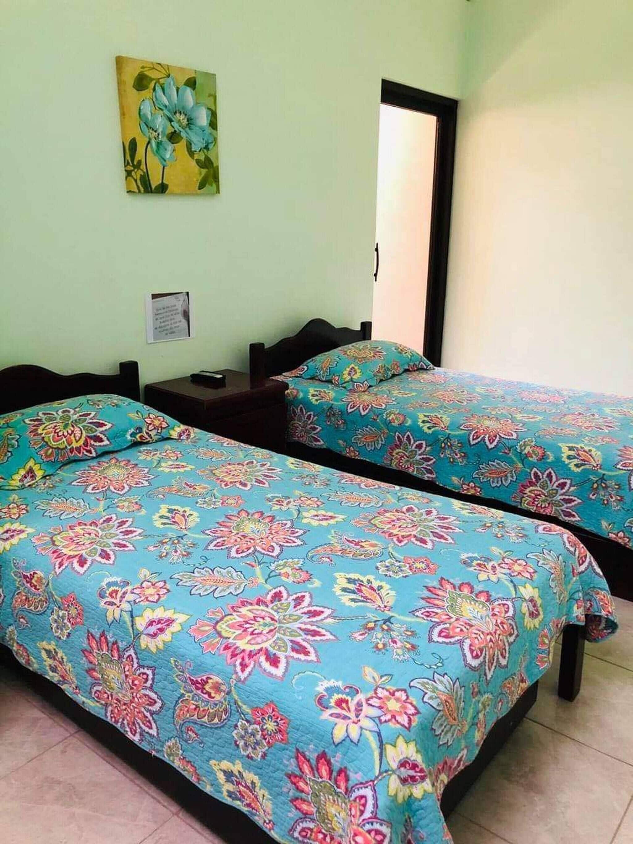 A room with two beds, a nightstand, a mirror, and a floral painting on the wall.