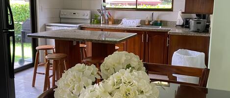 Una cocina con comedor, ventana con vistas y un florero con flores sobre la mesa.