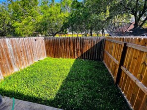 Ein umzäunter Garten mit Rasenfläche und Bäumen im Hintergrund.