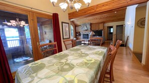 Uma sala de jantar com uma mesa posta para quatro pessoas, cadeiras de madeira e vista para a cozinha e a sala de estar ao fundo.